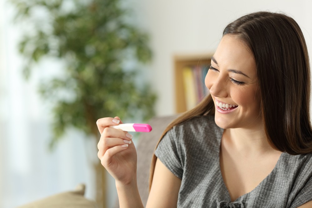 femme souriante qui regarde un test de grossesse positif