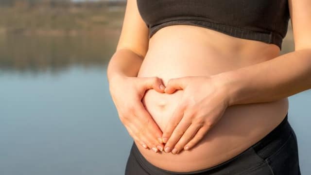 Femme tenant son ventre avec mains formant un cœur montrant comment se préparer à être enceinte avant conception