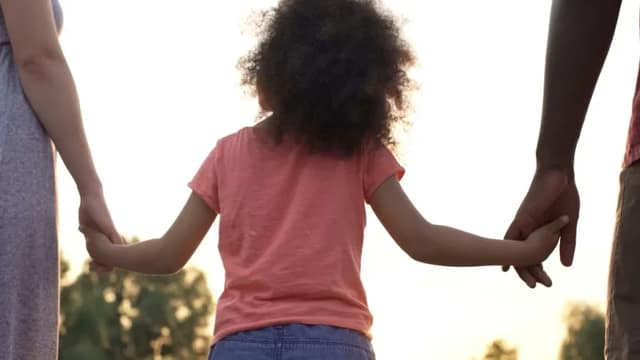 Petite fille tenant les mains de ses deux parents illustrant la coparentalité à distance et le lien familial