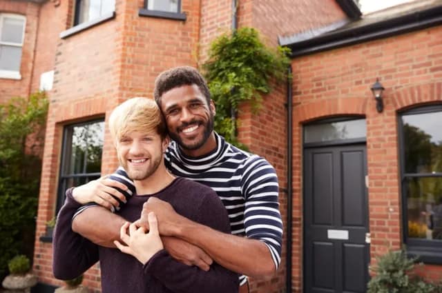 Couple d’hommes souriants devant leur maison relation homoparentale