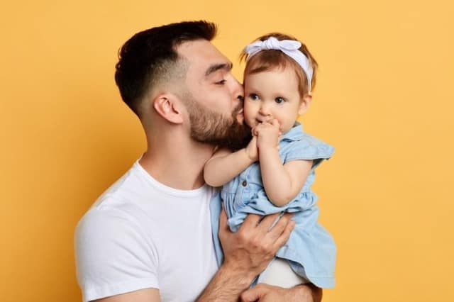 Père souriant portant sa petite fille dans les bras illustrant je veux être père et réalisation du désir de paternité
