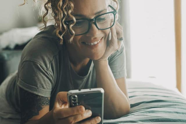 Portrait d'une femme heureuse et joyeuse, allongée sur le lit et utilisant un téléphone portable pour discuter et regarder des contenus en ligne. Des femmes modernes avec un smartphone. Bavarder avec des amis.