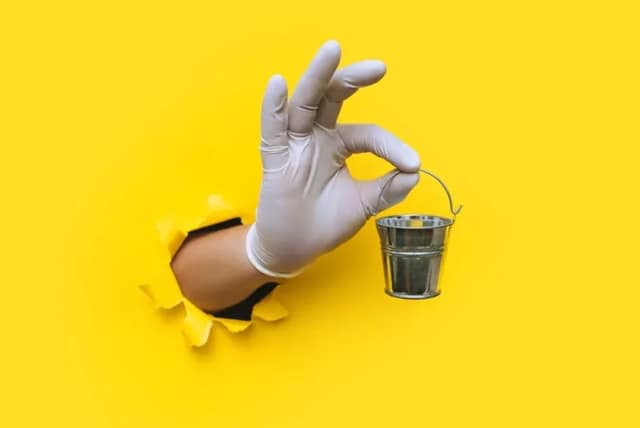 Main gantée portant petit seau avec liquide sur fond jaune représentant symboliquement don de gamètes pour procréation assistée