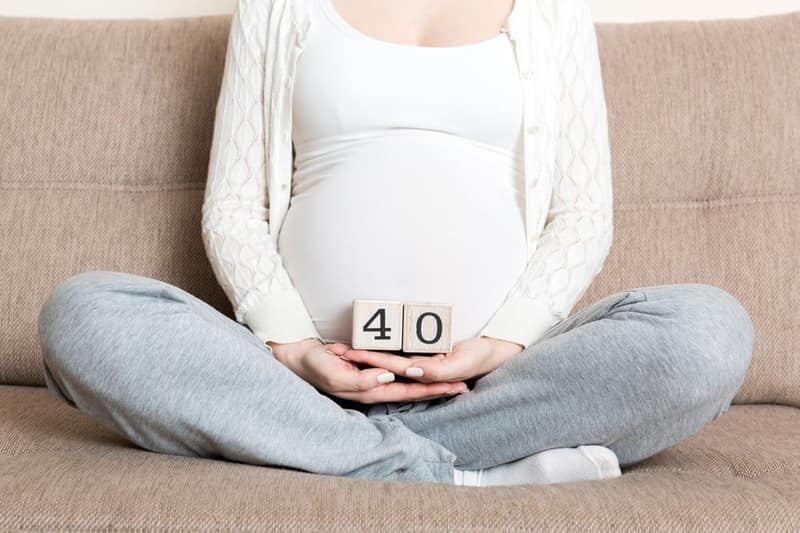 femme enceinte sur un lit tenant deux cubes indiquant 40 ans