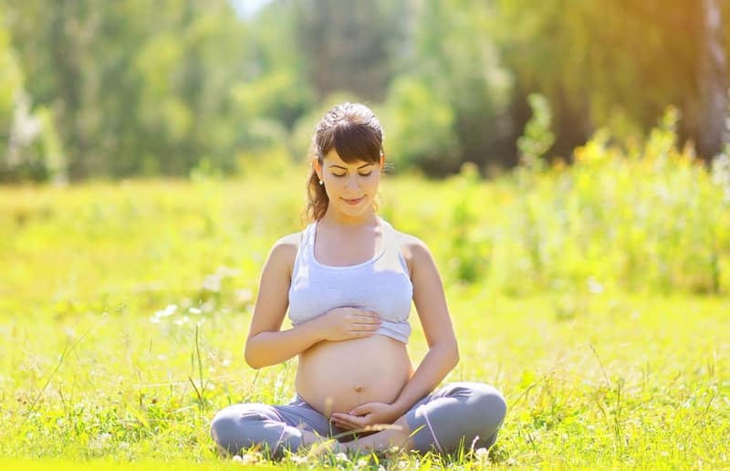 femme enceinte qui fait du yoga dans un champ