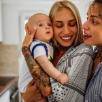 Portrait de deux jeunes femmes couple lesbien souriant avec leur bébé illustrant les droits parent social dans famille homoparentale