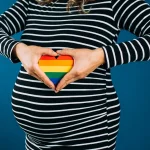 Femme enceinte tenant un cœur arc-en-ciel sur son ventre symbolisant la GPA en Europe pour couples LGBT