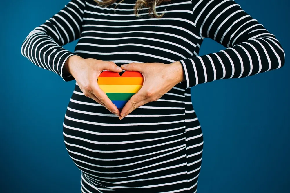 Femme enceinte tenant un cœur arc-en-ciel sur son ventre symbolisant la GPA en Europe pour couples LGBT