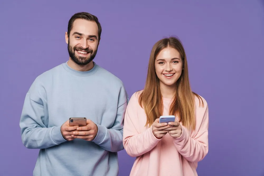 Homme et femme souriants tenant un smartphone, utilisant une app fertilité ensemble