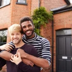 Couple d’hommes souriants devant leur maison relation homoparentale